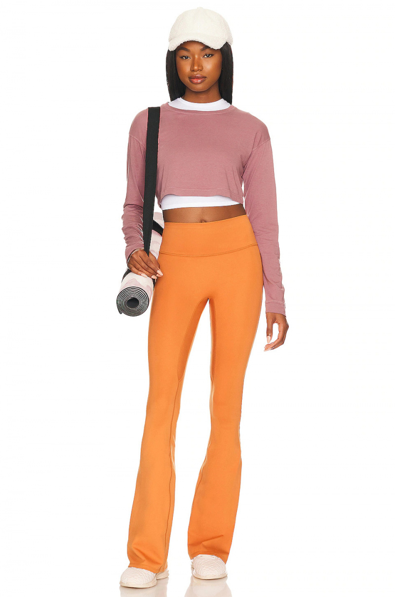   Pantalon de yoga évasé orange vif de la marque Well Being + Being Well. porté avec un haut à manches longues d'un rose discret.